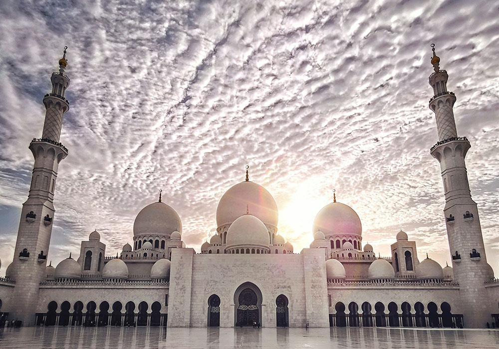 Panoramic view of Sheikh Zayed Grand Mosque with sun shining from behind