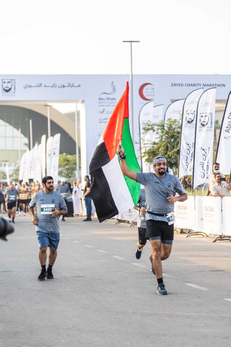 Man running with UAE flag at the Zayed Charity Marathon Abu Dhabi 2022