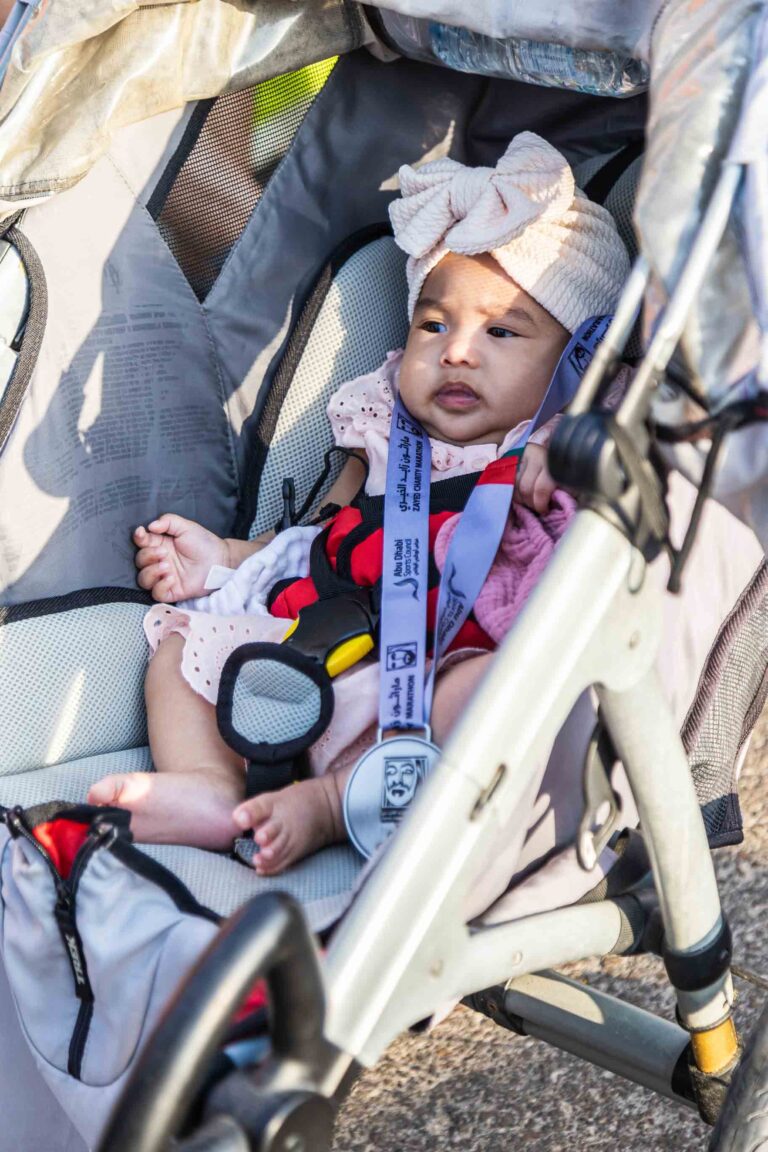 Baby in a stroller with a Zayed Charity Marathon Abu Dhabi 2022 completion medal around her neck